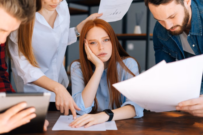 close-up-of-exhausted-overworked-young-business-woman-under-stress-at-office-colleagues-shaking-paper-documents-on-blurry-background-business-team-wants-to-get-answer-and-decision-from-boss-stockpack-istock Close-up of exhausted overworked young business woman under stress at office. Colleagues shaking paper documents on blurry background. Business team wants to get answer and decision from boss.
