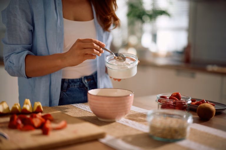 Close up of woman using Greek yogurt while making oatmeal at home.