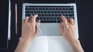 Directly above view, business woman hand typing on laptop computer with notebook digital tablet on office table, surfing the internet, searching the information, online research, e-learning