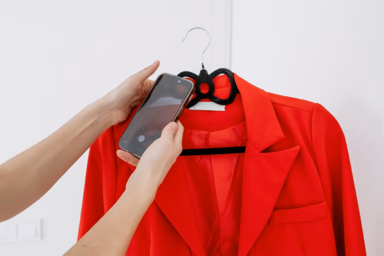 Female Hands Photographing Red Blazer on Black Velvet Hanger with Smartphone Against White Wall — Online Clothing Resale, Recommerce and Fashion Content Creation Concept