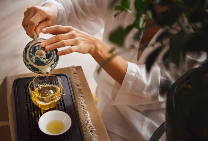 female-hands-pouring-tea-from-patterned-clay-teapot-into-clear-glass-pitcher-creating-serene-tea-ritual-soft-light-wooden-tea-tray-and-greenery-evoke-calming-mindful-chenese-ceremony-atmosphere-stockpack-istock Female hands pouring tea from patterned clay teapot into clear glass pitcher, creating serene tea ritual. Soft light, wooden tea tray and greenery evoke calming mindful chenese ceremony atmosphere.