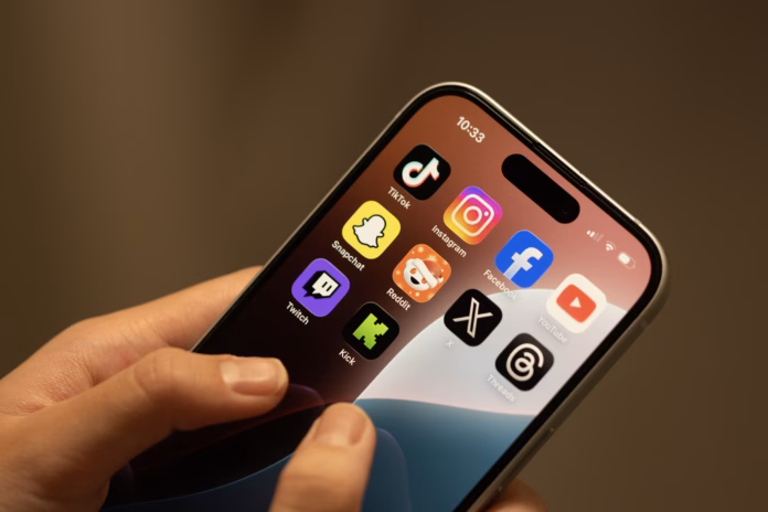Portland, OR, USA - Dec 18, 2025: Apps (TikTok, Instagram, Facebook, YouTube, Snapchat, Reddit, X, Threads, Twitch and Kick) included in Australia's world-first teen social media ban are seen on the screen of an iPhone held by a teenager.