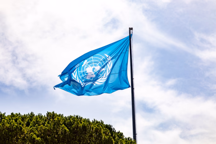 rome-italy-august-1-2021-flag-of-united-nations-against-blue-sky-the-olive-branches-are-a-symbol-for-peace-this-current-design-from-1946-a-revision-of-the-original-1945-design-and-colorrome-italy-augu-stockpack-istock Rome, Italy - August 1, 2021: Flag of United Nations against blue sky. The olive branches are a symbol for peace. This current design from 1946, a revision of the original 1945 design and color.Rome, Italy - August 1, 2021: Flag of United Nations and participating contries with UN building in Rome.Rome, Italy - August 1, 2021: Flag of United Nations and participating contries with UN building in Rome.