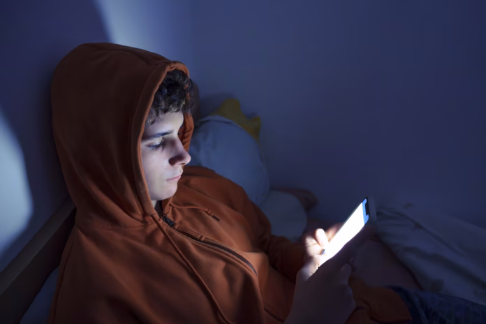 Teenager using a smartphone lying in bed late at night, playing games, watching videos online, and scrolling the screen. Children's screen addiction. Screen Addiction in Youth.