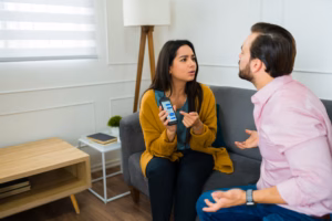 Latin woman looking angry showing text messages on the smartphone to her upset cheating husband